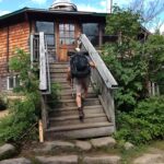 Hiker wearing pack climbs short staircase into a small wooden building