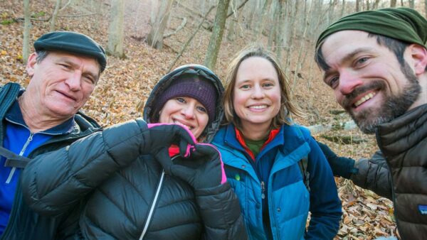 Sonu stands outdoors holding up hands in a heart shape, smiling with three other hikers