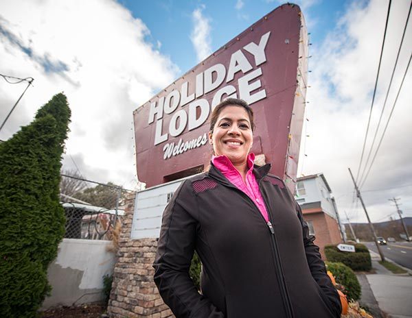 Sonu Chawla smiles at the camera, standing in front of large Holiday Lodge sign