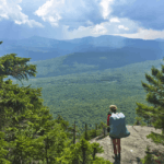 Hiker looks over a valley full of green trees