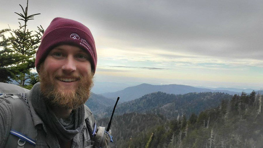 Ridgerunner smiles in a selfie with a backdrop of mountains and forest.