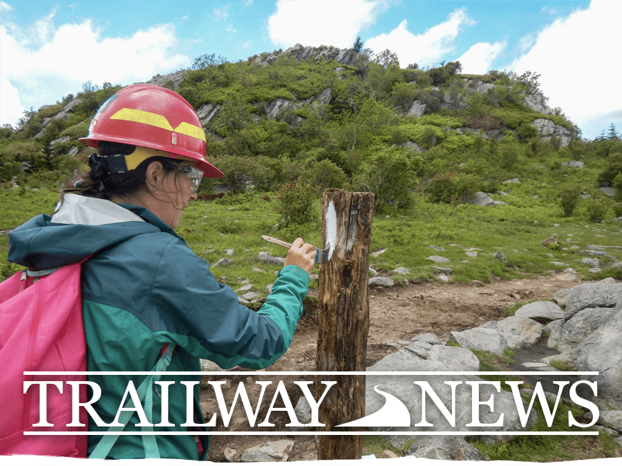 Trailway News header image, January 13, 2023. Image shows a volunteer painting a white blaze onto a wooden post with a green, rocky hill in the background.