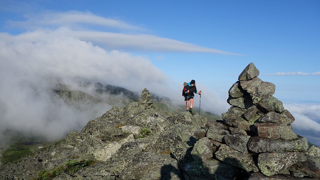 A hiker poses near a cairn atop a ridgeline