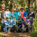Group of 11 Trail volunteers (mostly young adults) wearing hardhats and posing for the camera.