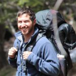 Greg Ritson headshot. In the photo, Greg smiles with a pack on his back.