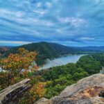 Photo by Alesha Donohue at the view from the Weverton Cliffs in Knoxville, MD. Photo shows cloudy grey skies over a river lined with colorful foliage.