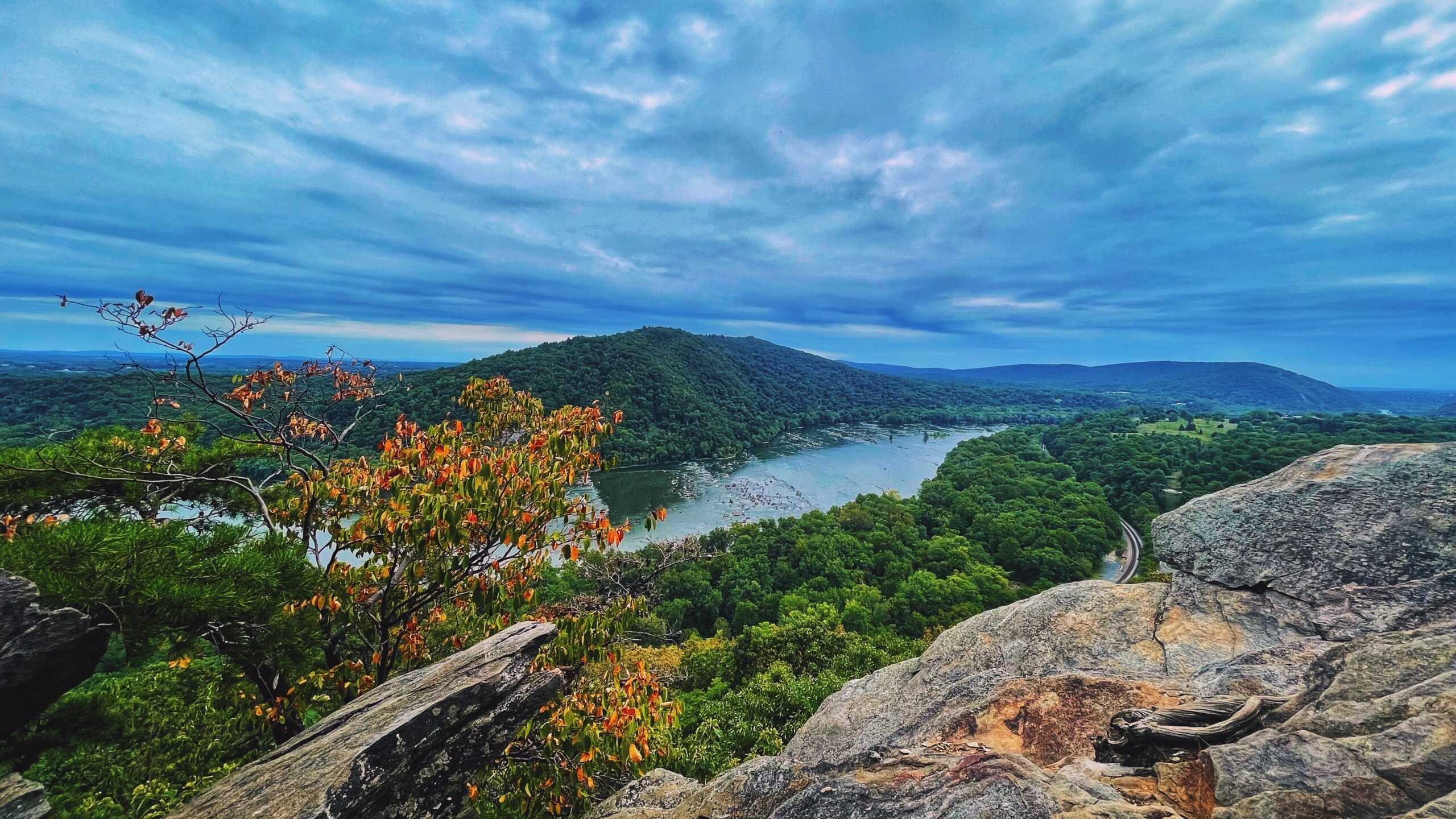 Photo by Alesha Donohue at the view from the Weverton Cliffs in Knoxville, MD. Photo shows cloudy grey skies over a river lined with colorful foliage.