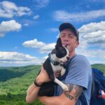 Hiker wearing cap and backpack holding Oreo the Boston Terrier
