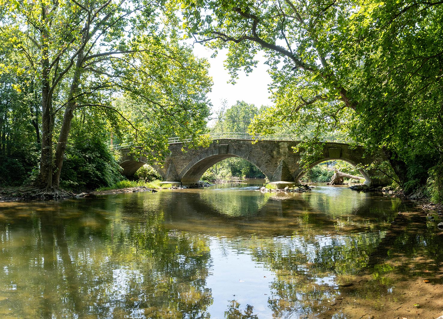Arched stone bridge over stream surrounded by trees