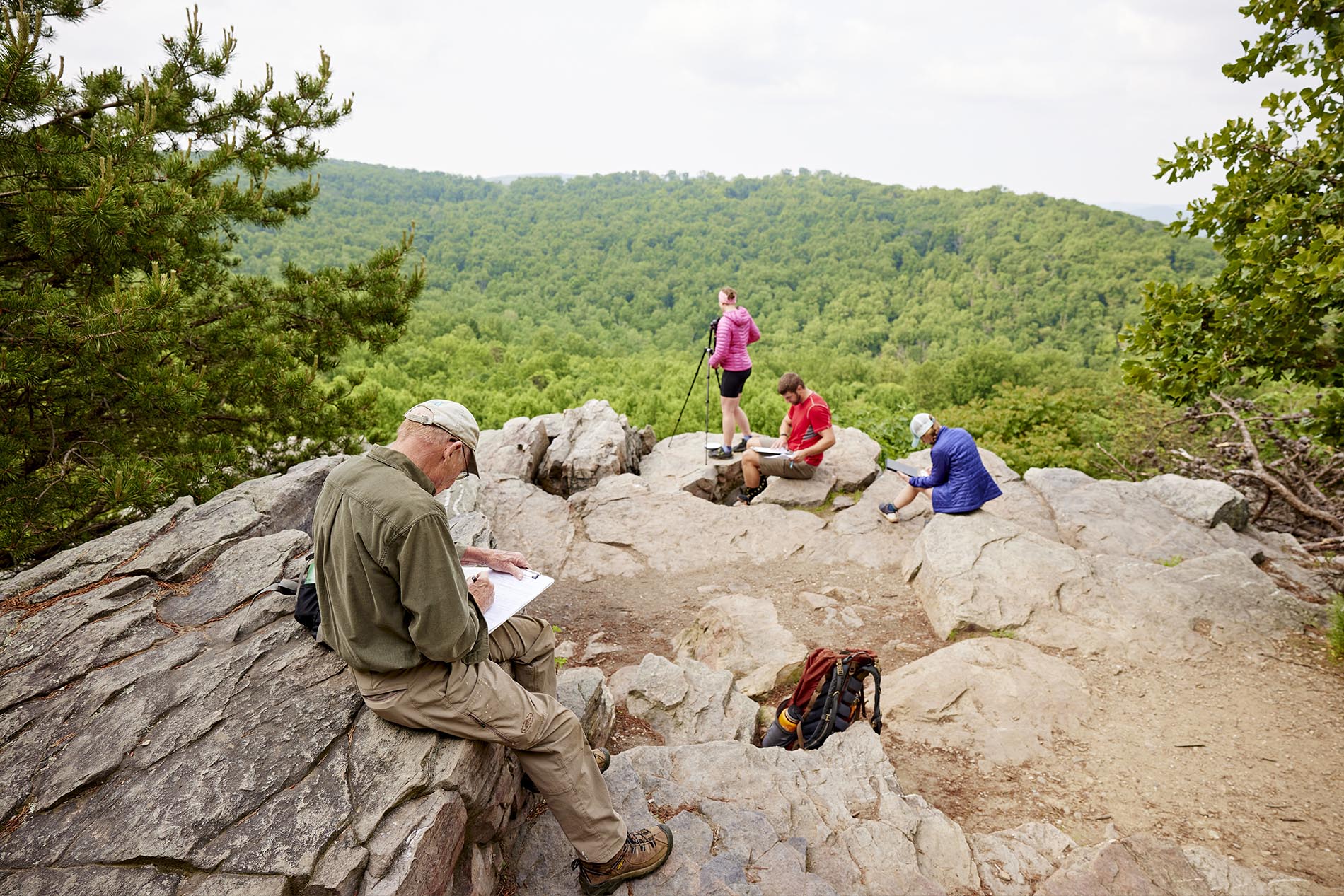 Four people on rocky overlook make notes about the view in front of them