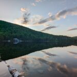 A glassy, still pond reflects the pastel blue sky