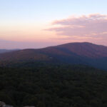 A dark mountain ridge against a pastel pink and blue sky