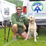 Man kneeling and smiling next to his service dog, a yellow lab