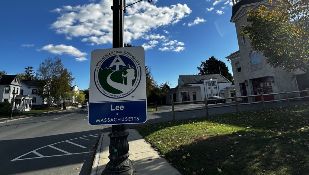 View of a street with a street sign in the foreground. The sign reads "Lee, Massachusetts"
