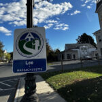 View of a street with a street sign in the foreground. The sign reads "Lee, Massachusetts"