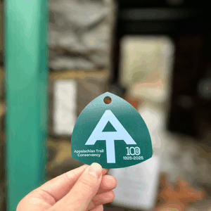Centennial ATC hangtag in pine green and mountain breeze blue with '100 Years' and AT symbol
