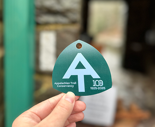 Centennial ATC hangtag in pine green and mountain breeze blue with '100 Years' and AT symbol