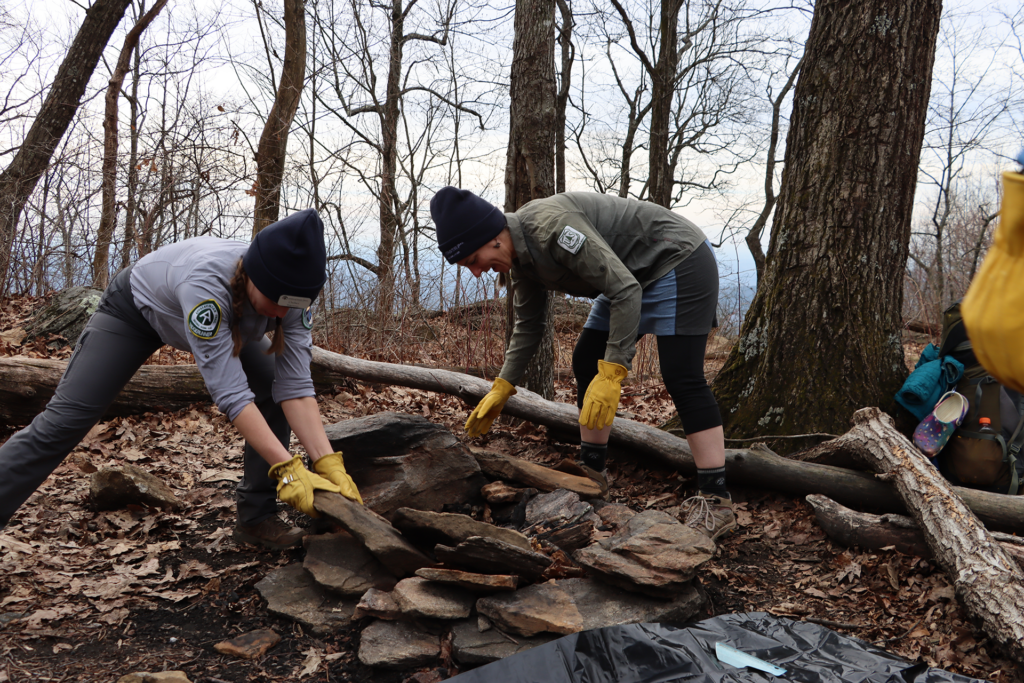 Two ridgerunners crouch to clean up a fire pit on the A.T. in Georgia