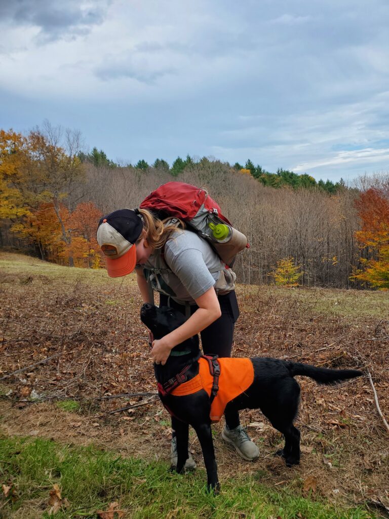 Photo by Ilana Goll of a hiker leaning over to pet a dog that is wearing a neon orange vest for visibility during hunting season