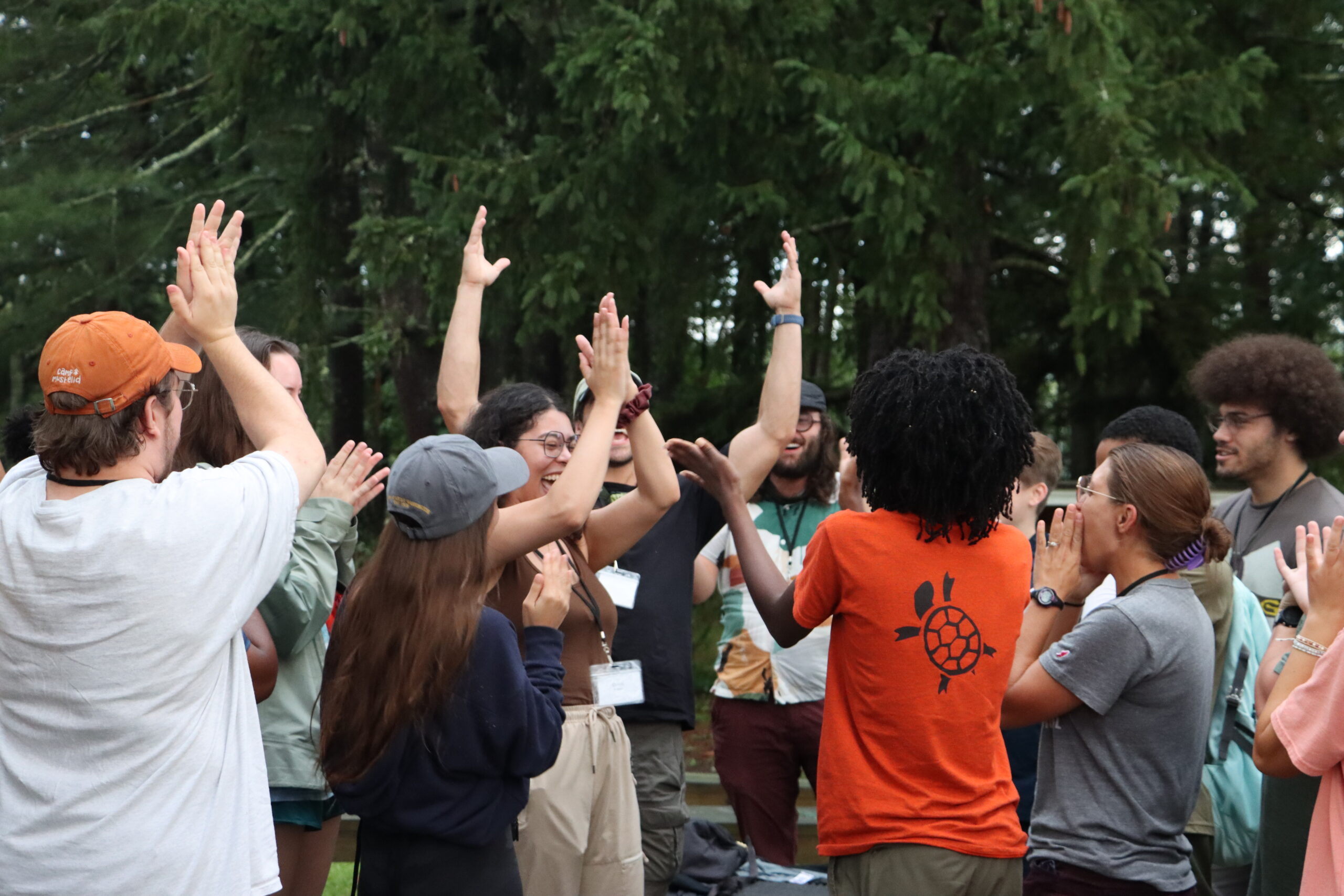 A bunch of young people crowded together excitedly with some of them holding their hands arms in the air, while playing a game.