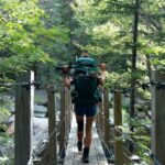 Hiker with pack crossing bridge over a forested stream