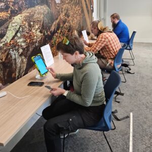 Three hikers sit at desks indoors, using iPads to digitally register for their hike.