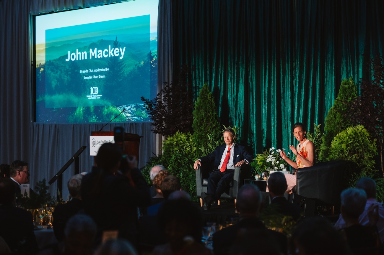 John Mackey and Jennifer Pharr Davis share the stage for a Fireside Chat, seated in front of green velvet drapes.
