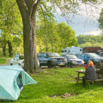 Five campers share a picnic table next to a light blue tent