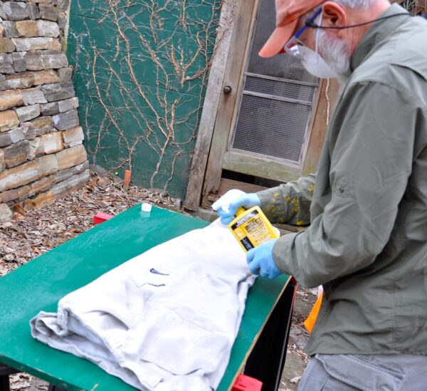 Person wearing mask and protective goggles sprays permethrin onto a hoodie.