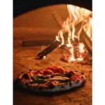 Pizza topped with red sauce and basil in a wood-fire stone oven