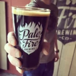 Man holding dark beer in a Pale Fire Brewing Company branded pint glass
