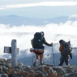 Two hikers wearing packs and A.T. hangtags overlook a misty vista on Bigelow Mountain