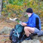 Bearded map sitting on a rock reading a paper map in the woods