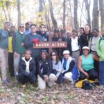 Group of nineteen hikes pose next to a signpost marking the Mason Dixon line on the Appalachian Trail.
