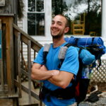 Hiker wearing blue t-shirt and large pack smiles at the camera