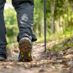 Close up leg and hiking boots walking through forest.