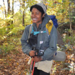 Female hiker holds hiking poles and smiles at camera