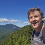 Jonathan Bird takes a selfie against a mountain backdrop in summer