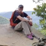 Volunteer Cindy Radich sits on a rock with a mountain view in the background