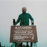 Jeff Hunter poses with Katahdin summit sign reading "Northern Terminus of the Appalachian Trail."