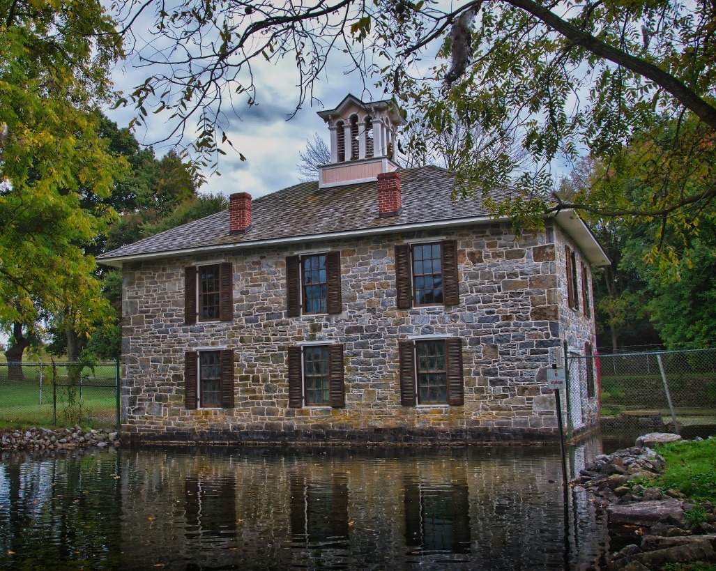 Historical two-story stone building stands next to a pond