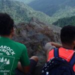 Two hikers overlook a scenic mountain vista.