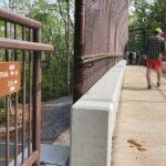 Two people walk across the McAfee Knob Trailhead Bridge past an Appalachian Trail sign.