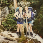 Hikers Hypo and Thermia smile and pose with their hiking gear. The ground is covered in patchy snow.