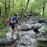 Hiker uses trekking poles to traverse large rocks along the Appalachian Trail.