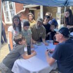 Small group gathers around Senator Tim Kaine as he signs books under a tent.