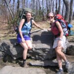 Two women hikers with large backpacks pose next to Springer Mountain's stone trail marker on the Appalachian Trail.