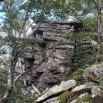 Large, jagged sandstone rock formation with sharp, geometric shapes extending from a tree-covered hillside.