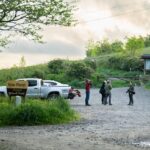 Group of hikers and a photographer stand on a gravel road near the Max Patch sign in Pisgah National Forest.