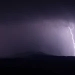 Lightning strike illuminating a dark stormy night over rolling hills and ridges.
